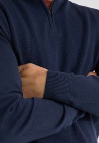 Marineblauwe zip-up pullover van textuurstof met geribde mouwen, voorzien van een halve kraag. Opvallend klein logo op de mouw.