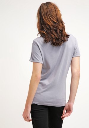 Camiseta de algodón gris de manga corta, con cuello redondo y puños de mangas enrollados. Textura suave con un ligero estiramiento, combinada con pantalones negros.