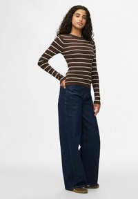 Maglia a maniche lunghe a costine marrone con righe crema, abbinata a jeans in denim blu scuro a gamba larga e calzature marroni. Design semplice e moderno.