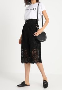 Černé krajkové culottes s propracovanými květinovými vzory, vysoký pas s knoflíkovým zapínáním. V kombinaci s bílým tričkem s potiskem a černými balerínami.