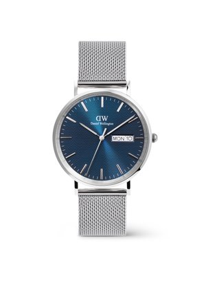 Zils pulkstenis ar sudraba stundu rādītājiem un datuma displeju; tam ir nerūsējošā tērauda acu josta un minimālisma dizains.