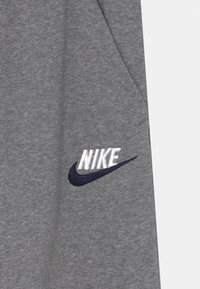 Grått tyg med en mjuk textur har en vit "NIKE"-logga och en marinblå swoosh, vilket visar en enkel design och tydlig varumärkning.