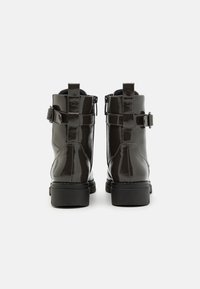 Stivaletti in pelle verniciata nera con finitura liscia, chiusura con zip e doppie cinghie con fibbie ai lati; tacco basso a blocco.