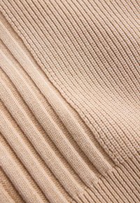 Gros plan d'un tissu en tricot côtelé beige montrant des lignes verticales et diagonales texturées ainsi qu'un matériau laineux doux.