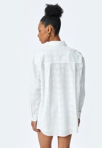 Hvid skjorte med diskret bladmønster, lange ærmer, knapkrave og afslappet pasform. Strukturert stof med en let følelse.