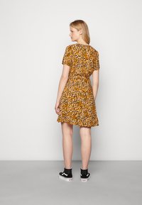 Vestido amarelo de manga curta com padrão de zebra em preto e castanho, saia rodada e cintura ajustada; combinado com sapatilhas em preto e branco.