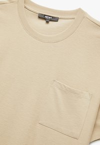 Beige bomulds T-shirt med rund hals, korte ærmer og en brystlomme. Struktureret stof med synlige syningsdetaljer.