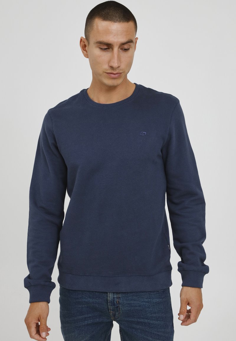 Navy blue sweatshirt made of cotton, featuring a crew neck, ribbed cuffs and hem, with a small logo on the chest. Worn with denim jeans.