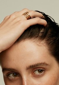 Anillos apilados en tono dorado que presentan un diseño liso y curvado con diferentes anchos y un pequeño detalle decorativo en el anillo superior.