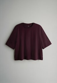 Burgundowa bluzka z krótkim rękawem, wykonana z miękkiej tkaniny, z okrągłym dekoltem i prostym wykończeniem z bocznymi rozcięciami dla łatwości ruchu.
