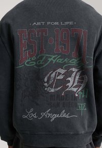 Black sweatshirt with vintage-style graphic text including "EST 1971," "Ed Hardy," "Los Angeles," and faded decorative elements on the back.