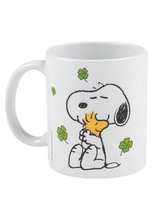 Weißer Keramikbecher mit einem Comic-Hund, der ein Stück Nahrung hält, umgeben von grünen vierblättrigen Kleeblättern. Glatte Textur, runde Form.