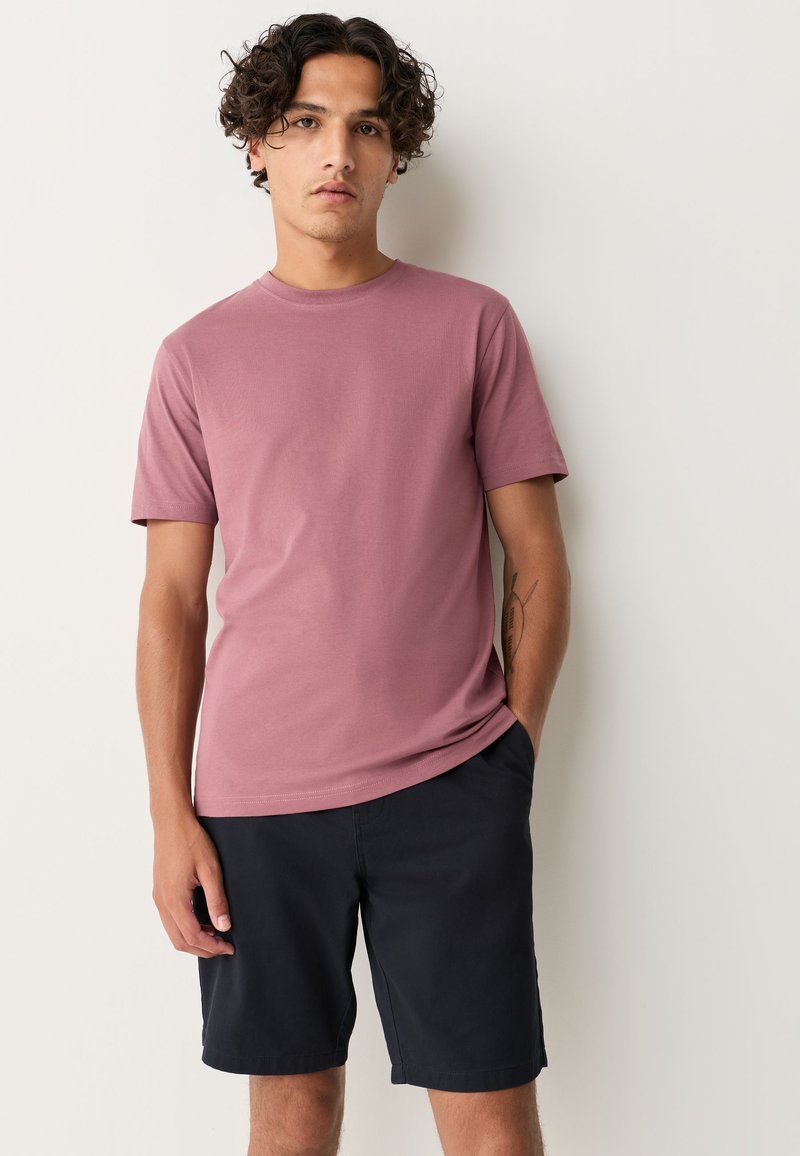 T-shirt med korte ærmer og rund hals i blødt mauvefarvet stof, kombineret med mørke, lette shorts. T-shirten har en glat tekstur og en afslappet pasform.