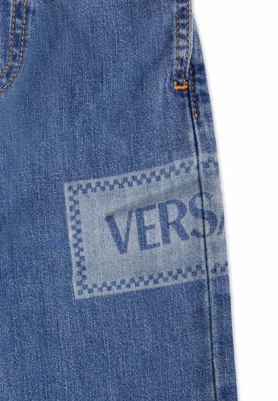 Tessuto denim di un blu chiaro con texture visibile. Presenta un grande etichetta quadrata che recita "VERSA" in un blu più scuro, bordata da un motivo cucito.