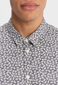 Camicia a maniche corte con sfondo blu navy e motivo a foglie bianche, colletto tradizionale e bottoni bianchi sulla patta.