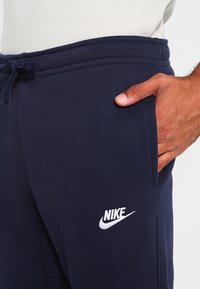 Pantalones de chándal de algodón color azul marino con cintura ajustable, bolsillos laterales y un logo blanco de Nike en el muslo izquierdo. Textura suave y diseño ajustado.