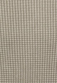 Beige gebreide stof met een gestructureerd houndstooth-patroon, met afwisselend lichte en donkere tinten. Het oppervlak is glad en gelijkmatig.