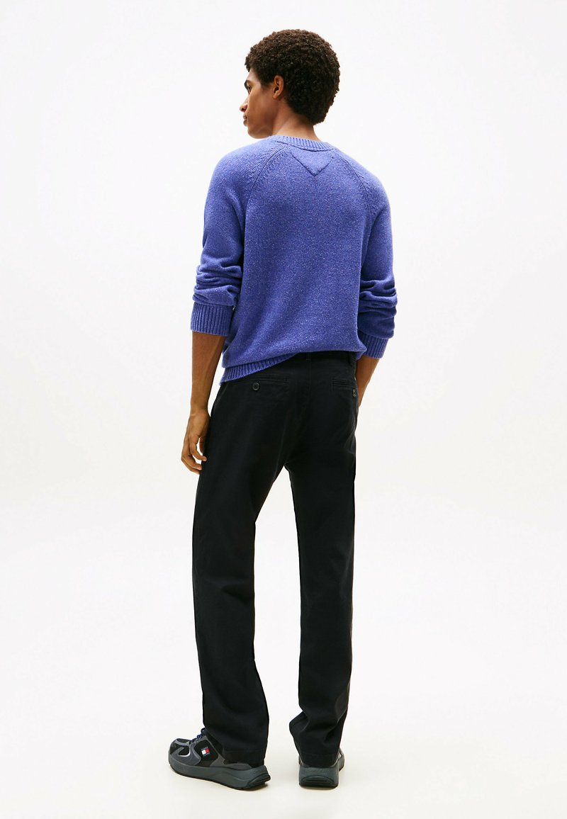 Pull en maille violet avec des poignets et un ourlet côtelés, associé à un pantalon noir et des baskets noires. La texture semble douce et décontractée.