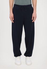 Navyblauwe sweatpants van zachte stof met een elastische tailleband en verstelbaar trekkoord. Gecombineerd met witte sneakers met een gladde textuur.