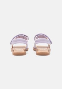 Lila sandaalit, joissa on takahihna ja avoin varvasosa, ruskealla kumipohjalla, korostaen sileää pintaa ja minimalistista tyyliä.