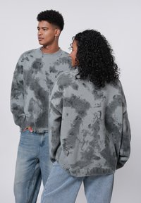Grå strikkede trøjer med et unikt abstrakt mønster, rund hals og ribbede kanter, parret med lyseblå jeans.