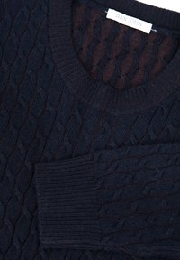 Granatowy sweter z fakturowanym wzorem w warkocze, z prążkowanym dekoltem i kieszonką na przedzie. Wygląd włóczki o fakturze.
