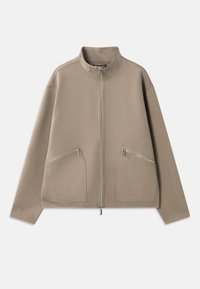 Chaqueta beige con cremallera fabricada en un tejido suave, que cuenta con dos bolsillos frontales con cremallera, un cuello alzado y un ajuste holgado con hombros caídos.