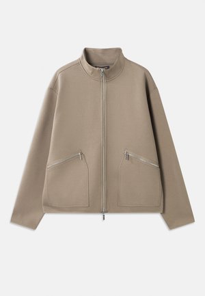 Beige zip-up jacket made of soft fabric, featuring two front zip pockets, a stand collar, and a relaxed fit with dropped shoulders.