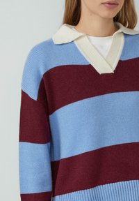 Strickpullover mit V-Ausschnitt, der abwechselnd blaue und burgunderrote Streifen aufweist, sowie einen cremefarbenen, gerippten Kragen. Glatte Textur.