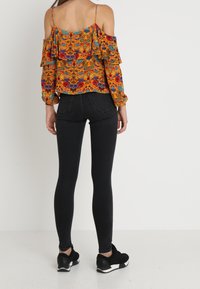 Haut orange à motif floral, à épaules dénudées, avec des accents à volants. Associé à un jean skinny noir et des chaussures de sport noires.