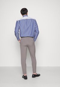 Skjorta med långa ärmar i blå och vita ränder, kombinerad med ljusgrå slim-fit-byxor och svarta loafers, sedd bakifrån.