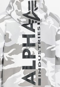 Szürke és fehér álcázású kapucnis pulóver, amelyen nagy fekete betűs grafika olvasható: "ALPHA INDUSTRIES" a hátsó részen. Pamut keverék anyag.