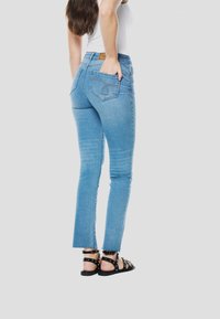 Lichtblauwe slim-fit jeans met achterzakken, lichte vervaging en een onafgewerkte zoom. Gecombineerd met zwarte sandalen met studs.