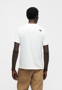 Λευκό βαμβακερό μπλουζάκι με κοντά μανίκια και στρογγυλή λαιμόκοψη. Φέρει μαύρο λογότυπο στην άνω πλάτη. Φοριέται με χακί παντελόνι.