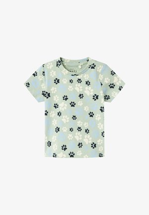 Camiseta de manga corta para niño pequeño de color verde claro con un patrón de huellas en negro, blanco y azul.
