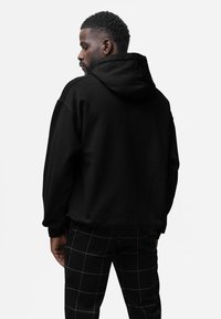 Sort hætte sweatshirt med en afslappet pasform, der har et struktureret stof og kengurulomme, parret med ternede sorte og hvide bukser.