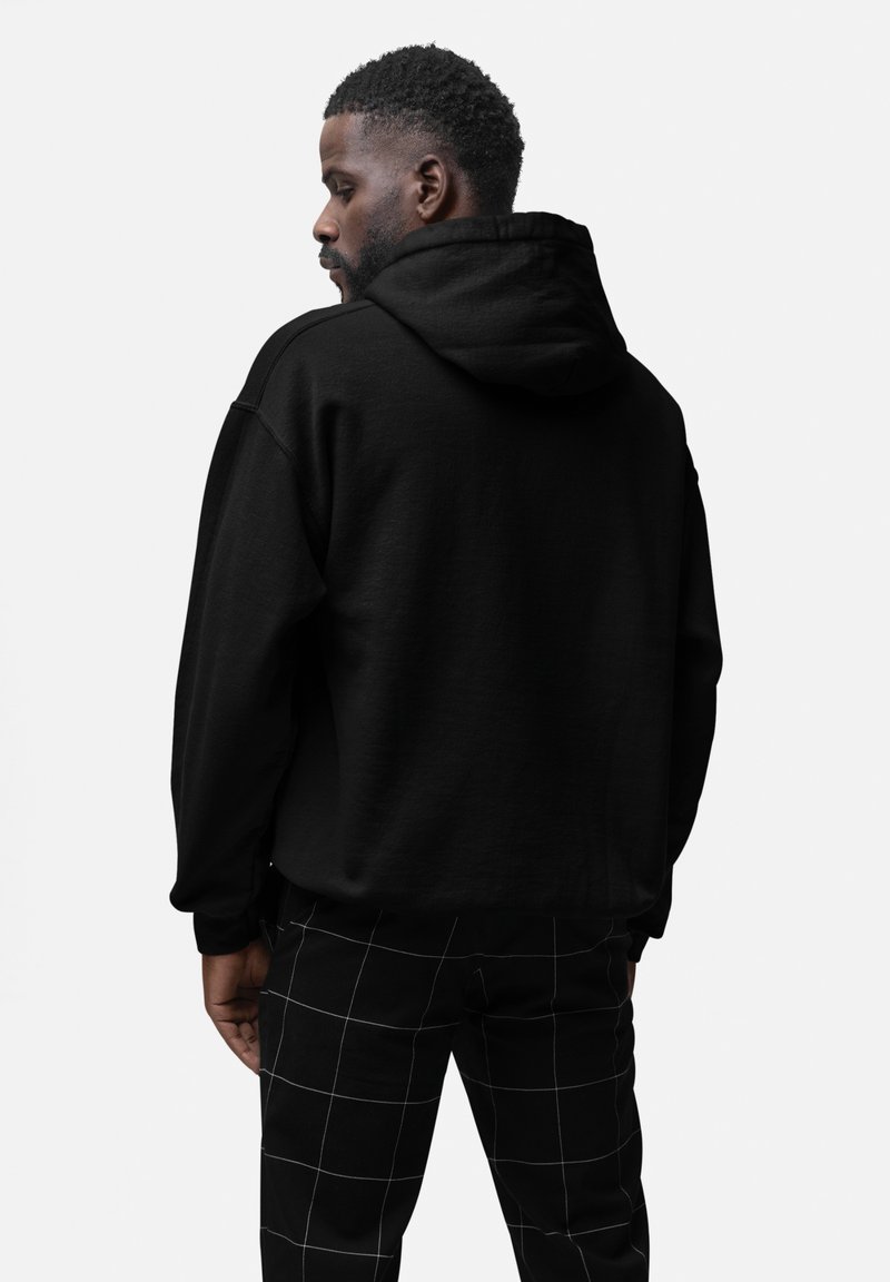 Sort hætte sweatshirt med en afslappet pasform, der har et struktureret stof og kengurulomme, parret med ternede sorte og hvide bukser.