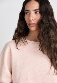 Lichtroze sweatshirt met een zachte textuur, met een ontspannen pasvorm en een subtiele gespikkelde print. Ronde halslijn en verlaagde schouders.