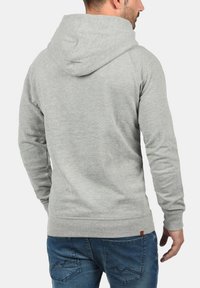 Szara bluza z kapturem, wykonana z miękkiego materiału, z tylnym kapturem, ściągaczami przy mankietach i w pasie. Zestawiona z niebieskimi dżinsami.