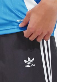 T-shirt de sport bleu avec des accents blancs et l'étiquette "AEROREADY", associé à un short noir arborant trois bandes blanches et un logo Adidas.