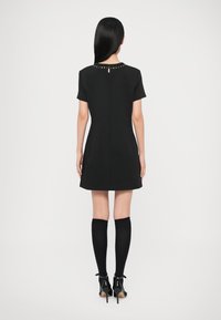 Černé šaty s krátkými rukávy a přiléhavým střihem, s kulatým výstřihem, výřezem na zádech ve tvaru klíčové dírky a zlatými ozdobnými nýty.