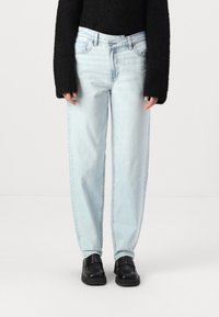 Vaaleansiniset farkut rentoa istuvuutta, joissa on viisi taskua ja keskikorkea vyötärö. Yhdistetty mustiin liukuviin kenkiin.