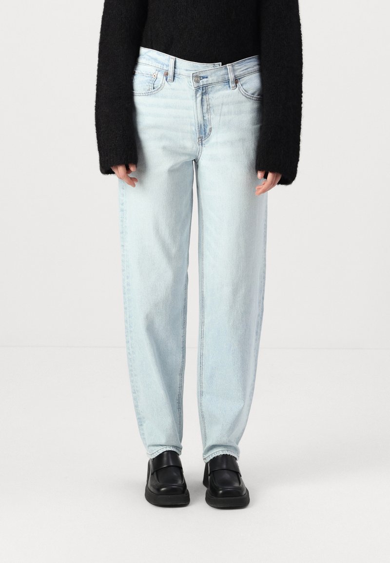 Vaaleansiniset farkut rentoa istuvuutta, joissa on viisi taskua ja keskikorkea vyötärö. Yhdistetty mustiin liukuviin kenkiin.