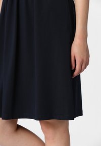 Navy blue, knee-length dress with a soft, smooth texture; gathered waist and straight hem. Includes a hand resting on the fabric.