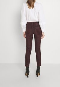 Burgundské slim kalhoty vyrobené z měkké tkaniny, s středně vysokým pasem, zadními kapsami a elegantním střihem. Doplněné černými botami na podpatku.