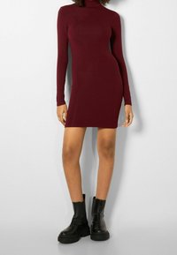 Bordó bodycon šaty s dlouhými rukávy a stojáčkem u krku. Nošeny s černými robustními kotníkovými botami s bočním zipem a texturovanou podrážkou.