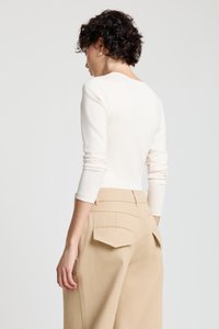 Haut crème à manches longues avec un dos échancré, associé à un pantalon beige taille haute avec deux poches arrière et un tissu texturé.