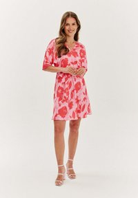 Růžové šaty s volným střihem, zdobené květinovým vzorem v tmavších odstínech růžové. Krátké rukávy a nařasený pas vytvářejí splývavý siluetu.