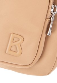Beżowa nylonowa torba z teksturowaną powierzchnią, wyraźnym logo "B" oraz srebrnymi elementami i zamkiem błyskawicznym.