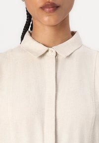 Heledbeez linane särk klassikalise krae, ühe nupuga kinnituse ja peene tekstuuriga, millel on puhas ja minimalistlik disain.